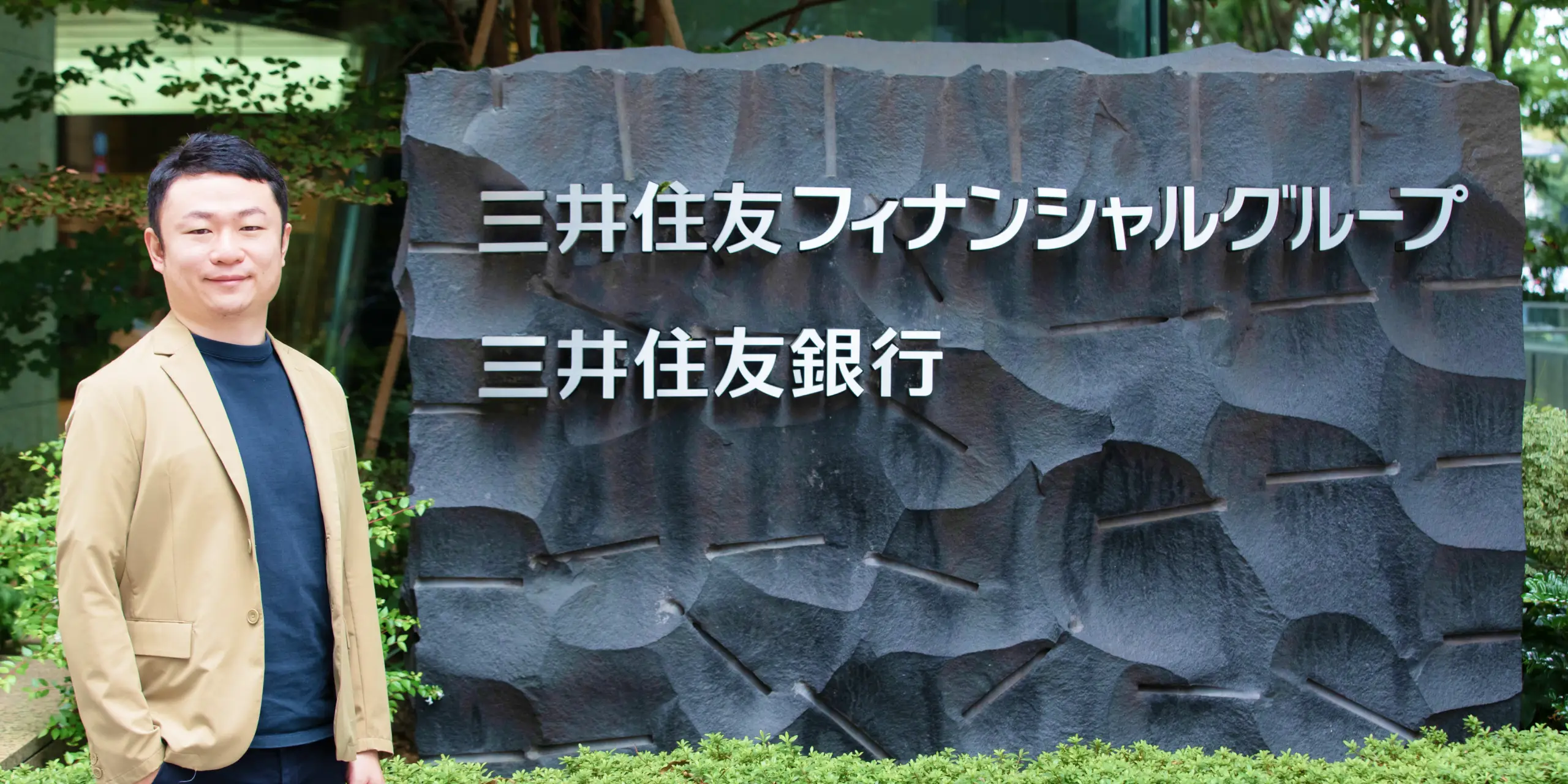 三井住友フィナンシャルグループ、三井住友銀行の会社銘板を背景に立つ柳澤隆大氏の写真